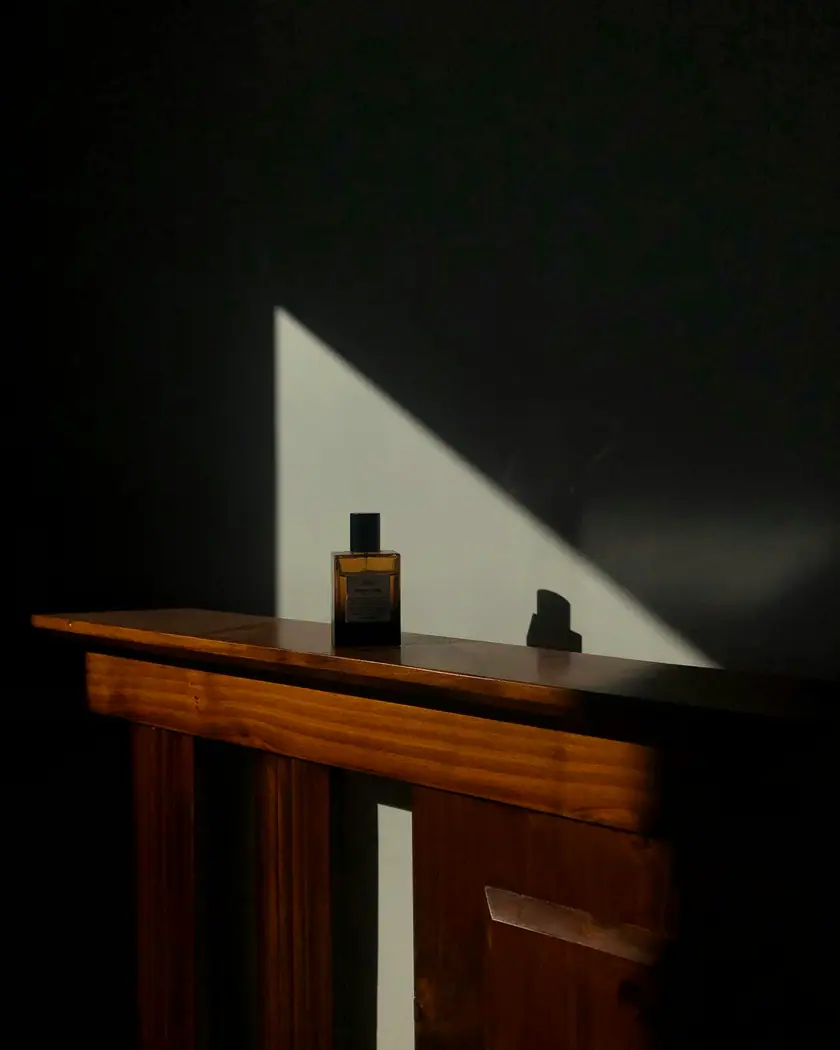 Frasco de perfume oscuro sobre una consola de madera atravesada por un haz de luz
